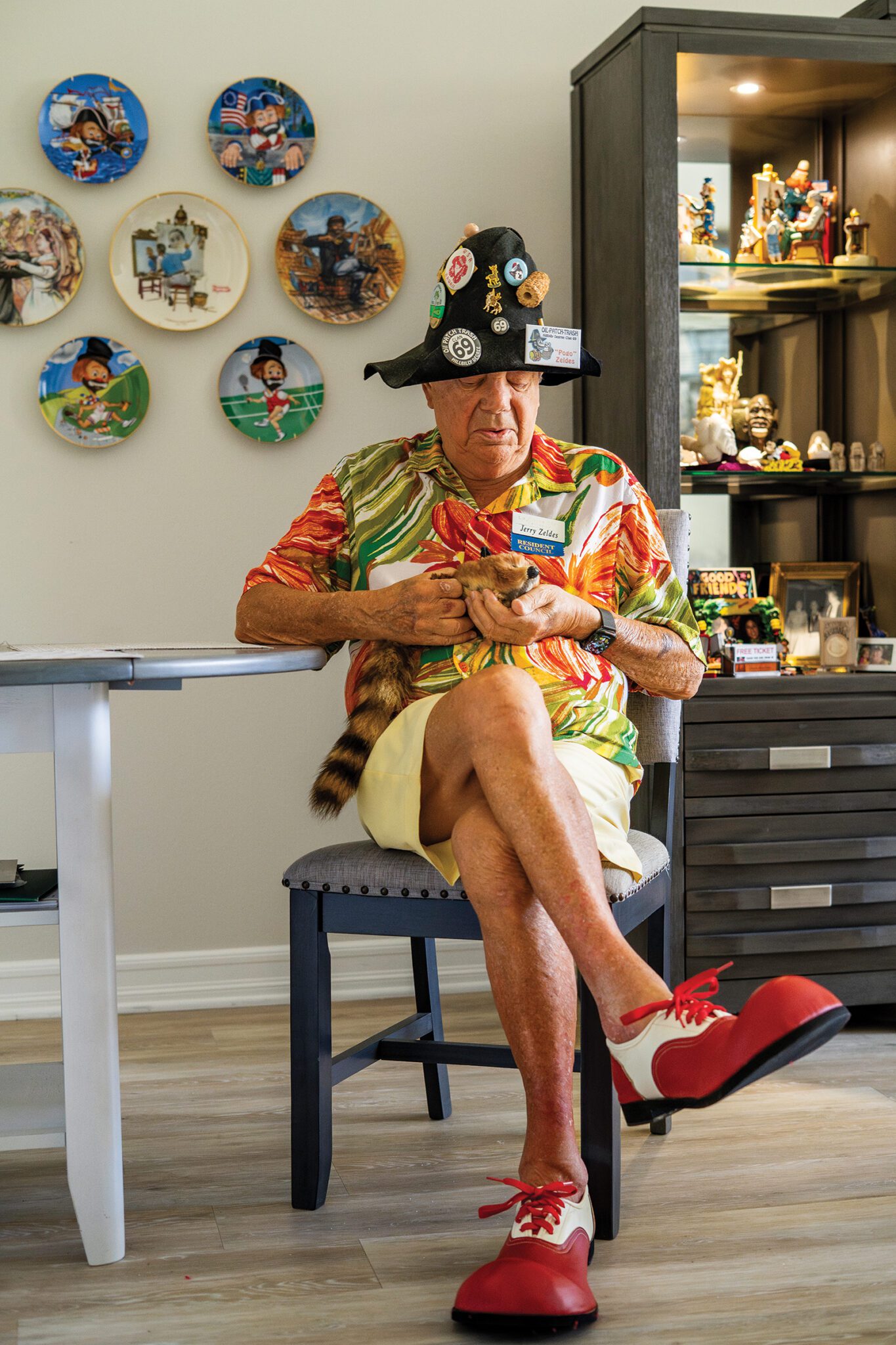 Jerry Zeldes sports his clown shoes while relaxing at home with rocky the raccoon, a trick stuffed animal.